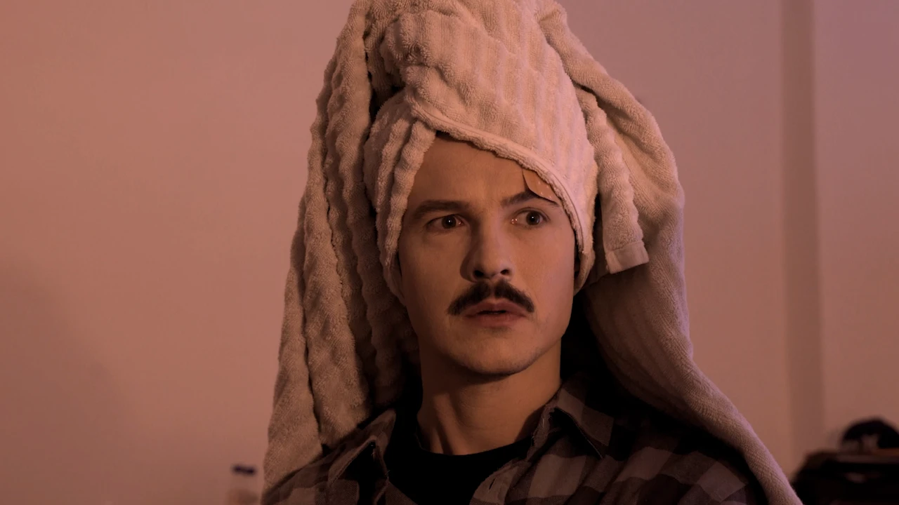 A man with a moustache and a towel on his head looks baffled.