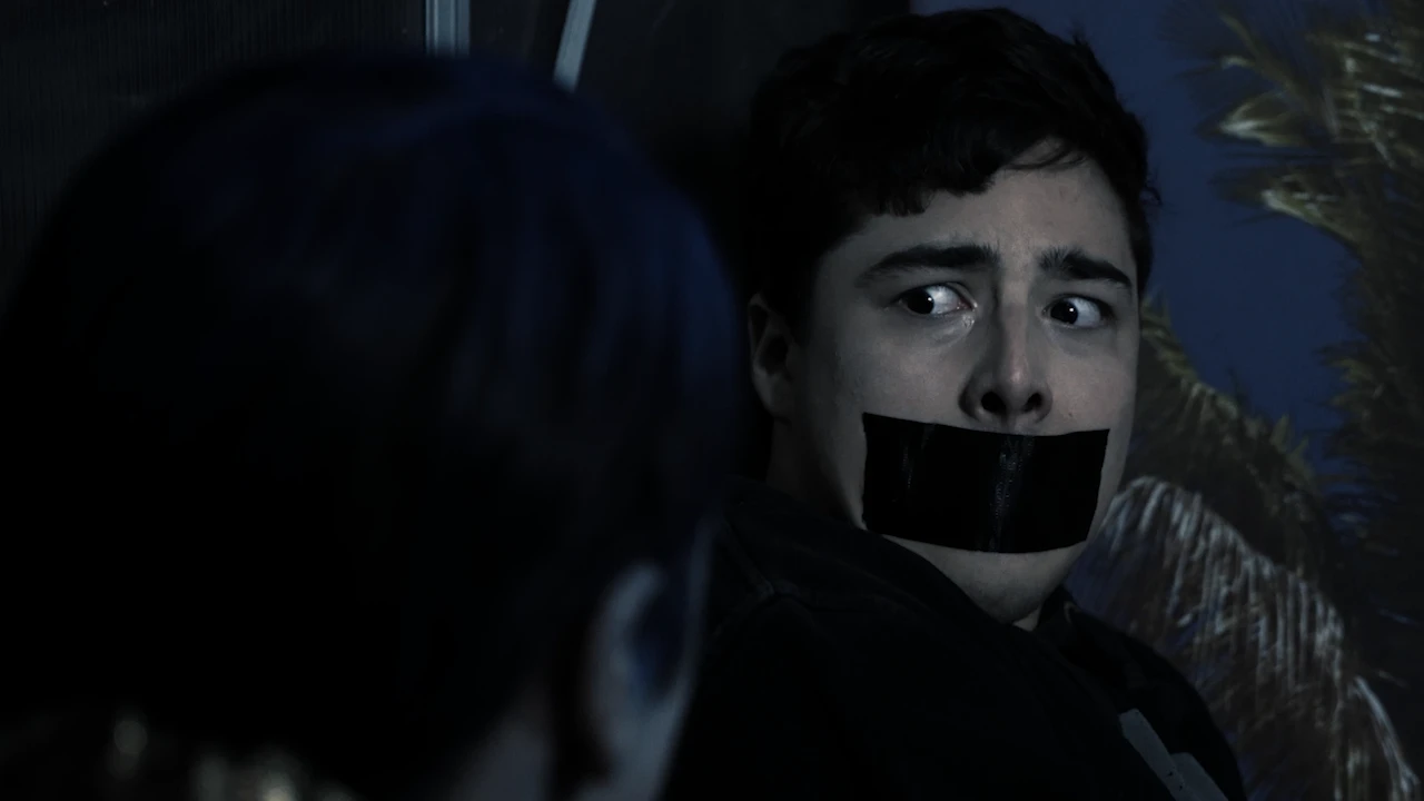 A young man with tape over his mouth glances sideways in fear.